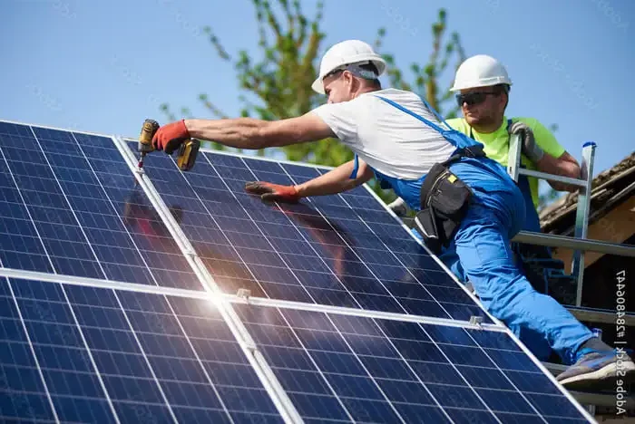 Professional solar panel installers fitting rooftop panels on a sunny day in the UK."