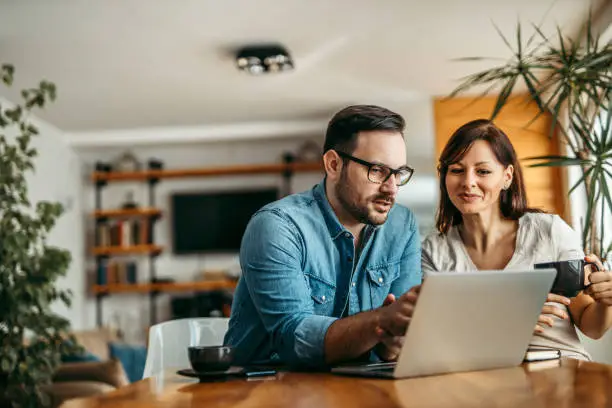 A smiling couple reviewing flexible boiler finance options on a laptop at home, seated at a wooden table in a bright, modern living space.
