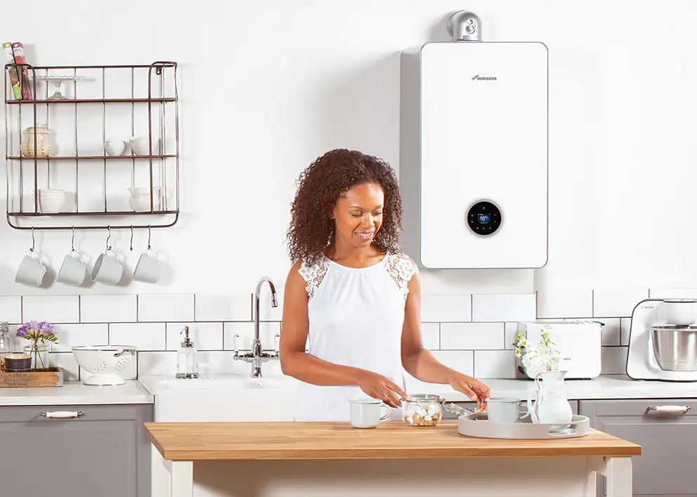 Woman standing in a modern kitchen preparing tea beneath a wall-mounted Worcester boiler, highlighting a clean and efficient boiler installation setup.
