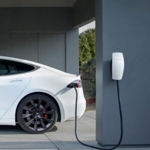 Tesla vehicle charging via a wall-mounted Tesla home charger on a private driveway, with a modern garage backdrop.