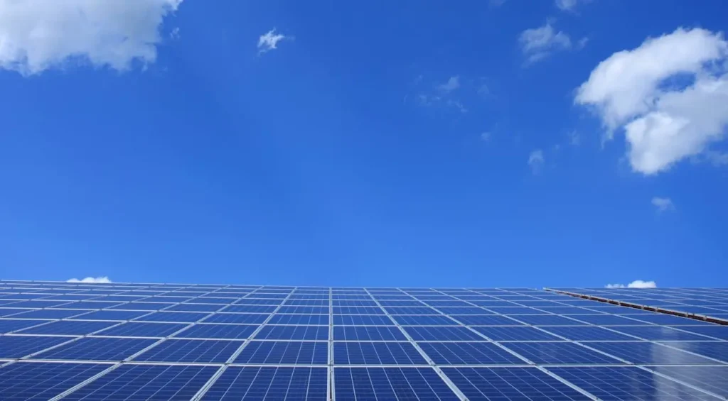 Low-angle view of a solar panel array beneath a clear blue sky with scattered clouds.